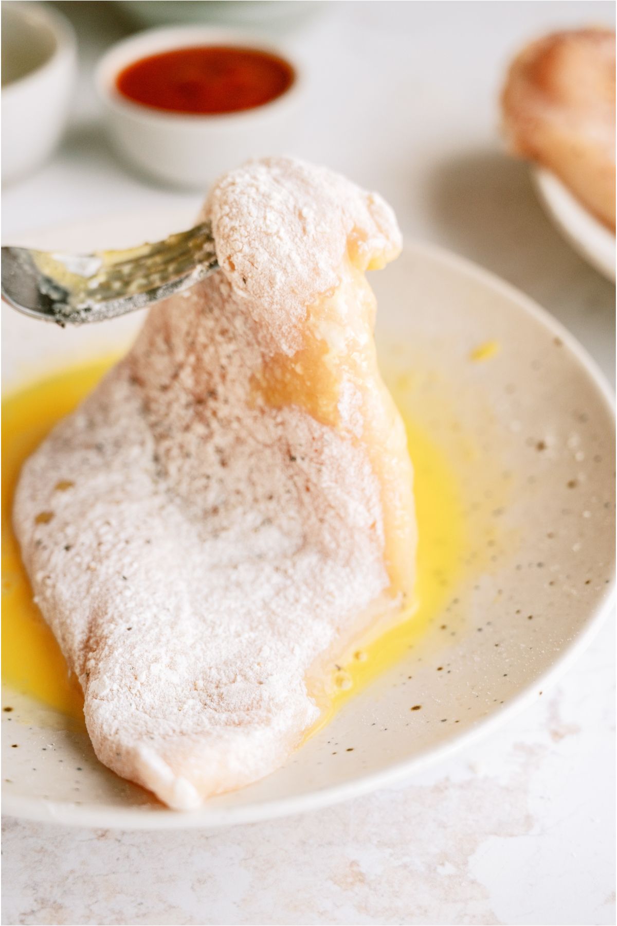 Using a fork to dip a floured chicken breast in egg.