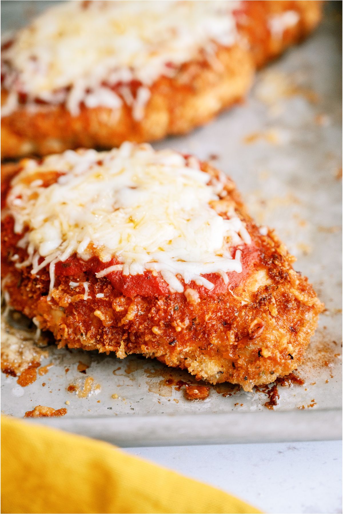 Chicken Parmesan on a baking sheet with other Chicken Parmesan Breasts in the background.