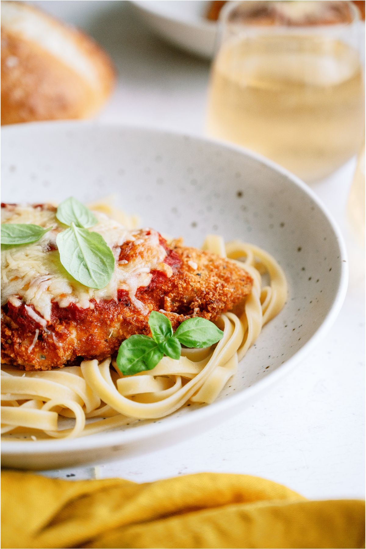 A white bowl filled with pasta and topped with Chicken Parmesan with fresh herbs.