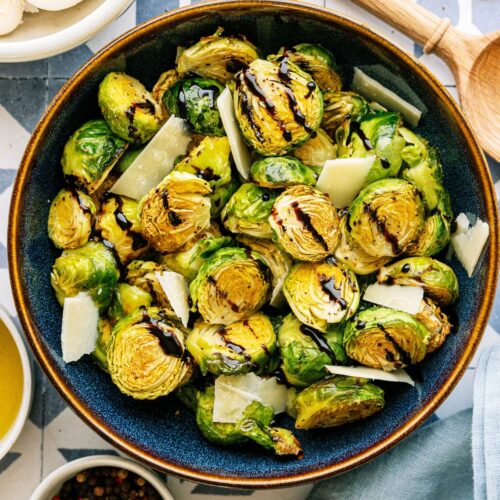 A large bowl of Crispy Air Fryer Brussel Sprouts drizzled with balsamic glaze with a wooden spoon on the side.