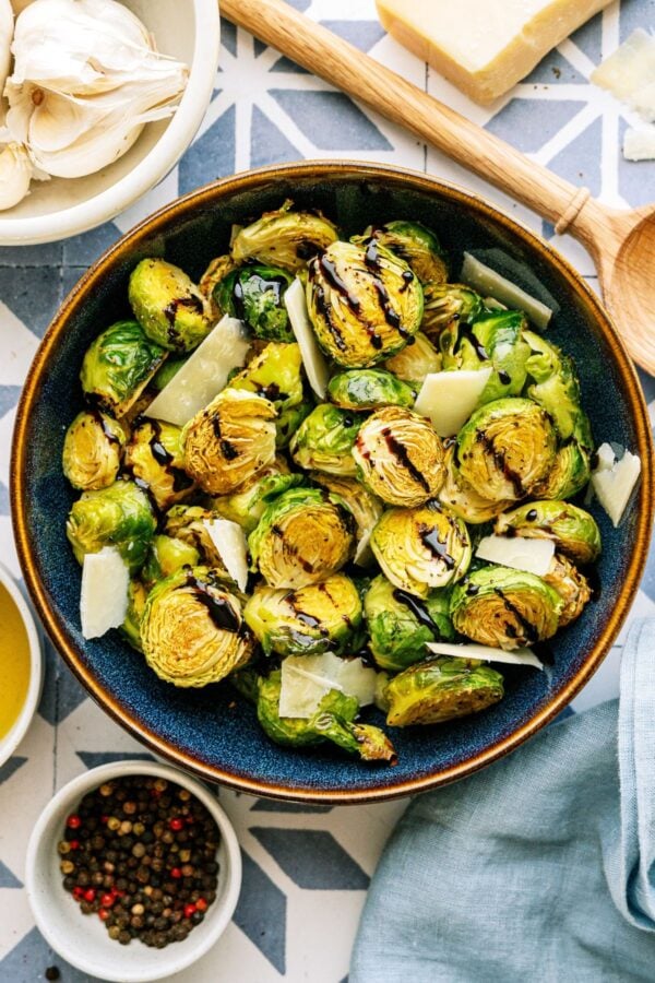 A large bowl of Crispy Air Fryer Brussel Sprouts drizzled with balsamic glaze with a wooden spoon on the side.