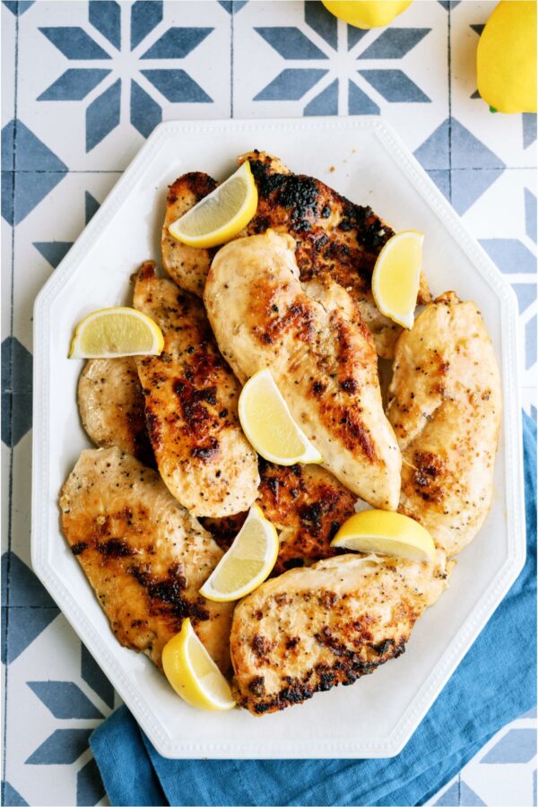 A plate full of cooked chicken breasts with slices of fresh lemons.