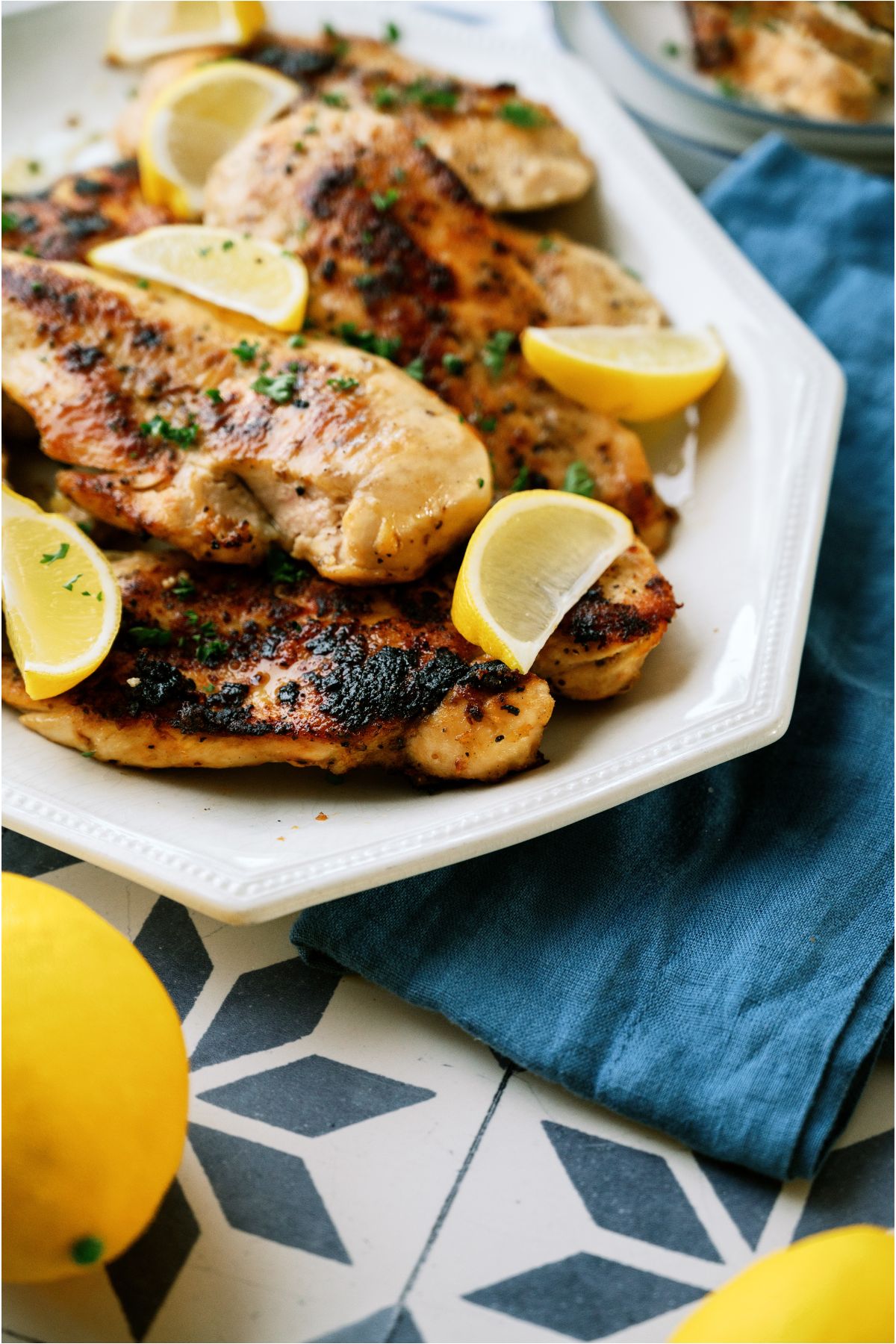 Lemon Pepper Chicken on a serving plate with lemon wedges and fresh lemons around the serving plate. Plate is on a blue towel.