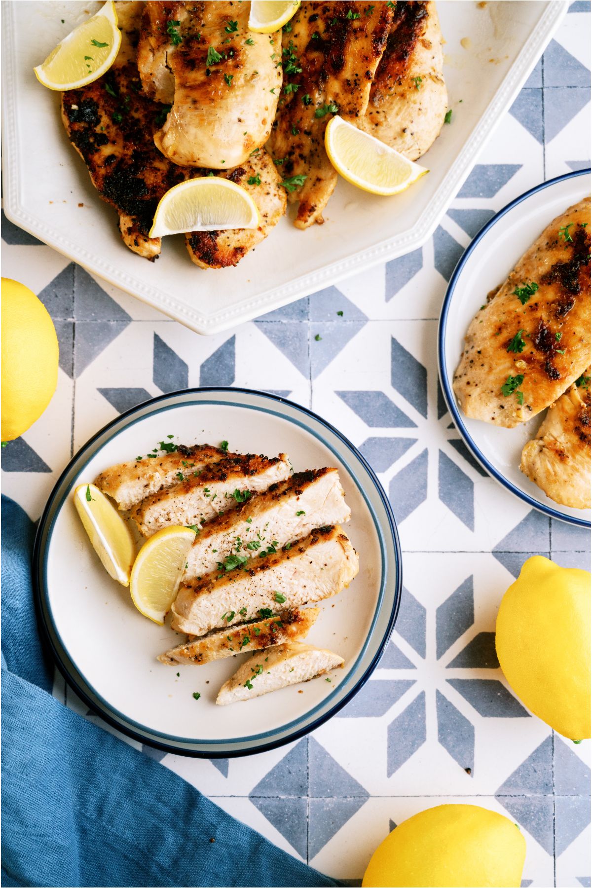 Top view of a serving plate with Lemon Pepper Chicken and lemon wedges and a small plate with a sliced Lemon Pepper Chicken breast.