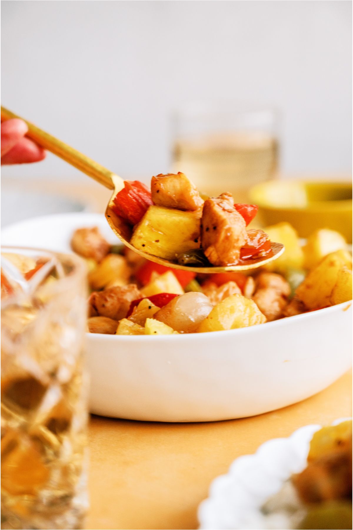 A spoon lifting a scoop of Sheet Pan Hawaiian Chicken out of a serving bowl.