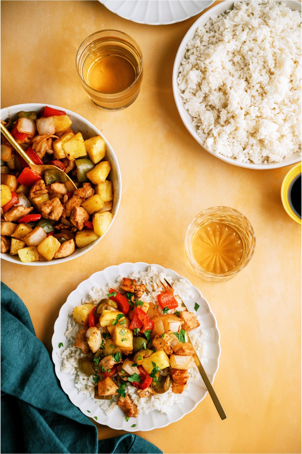 Top view of a serving bowl of Sheet Pan Hawaiian Chicken, a serving bowl of white rice and a plate of rice topped with Sheet Pan Hawaiian Chicken with a fork.