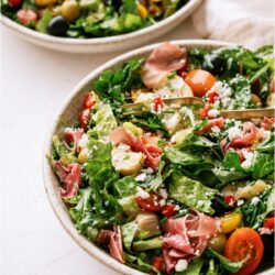 2 bowls of Antipasto Salad on a white background. One bowl has a fork.