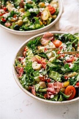 2 bowls of Antipasto Salad on a white background. One bowl has a fork.