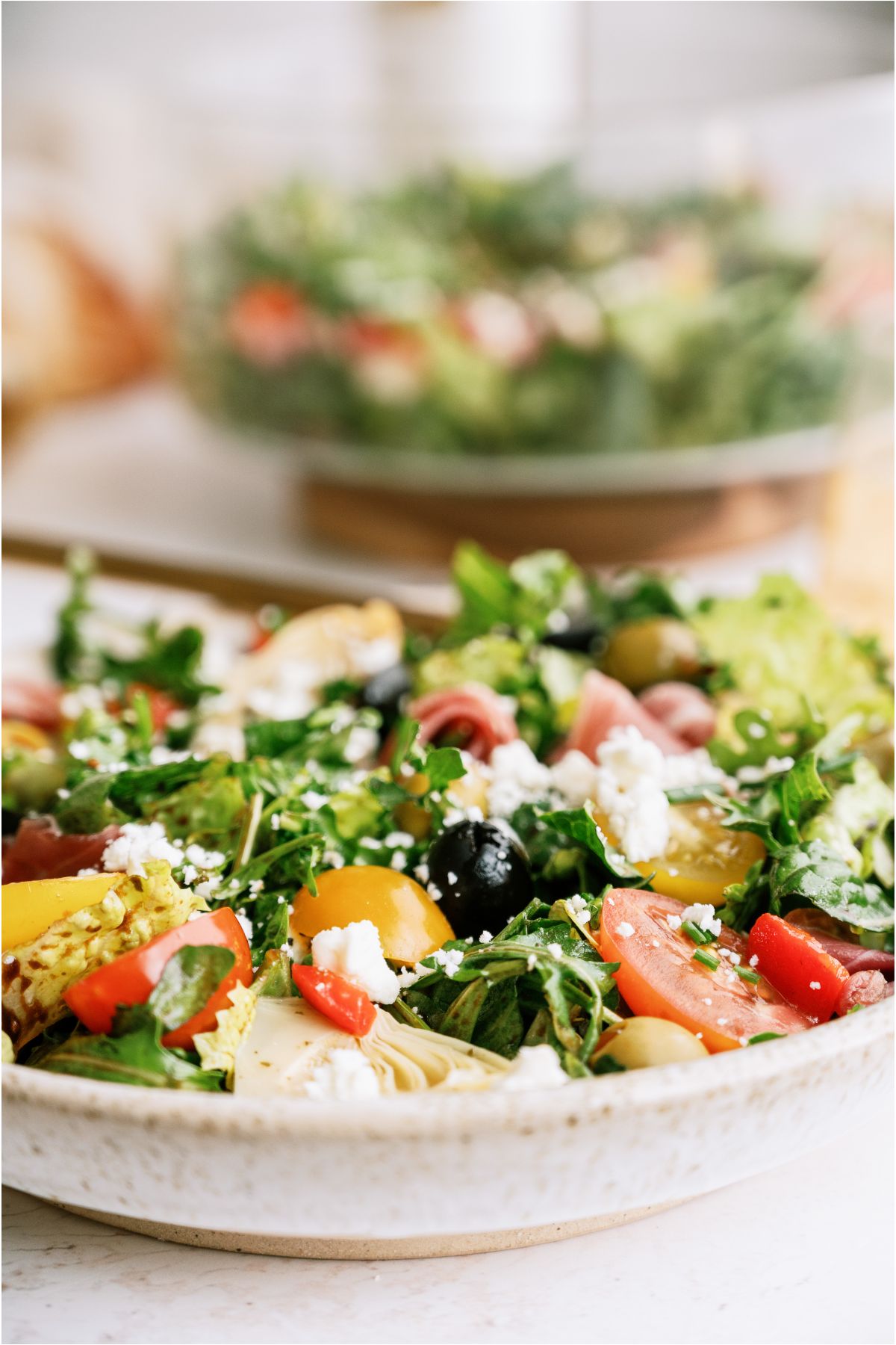 Close up view of a bowl of Antipasto Salad with a fork. Another bowl of Antipasto Salad in the background.