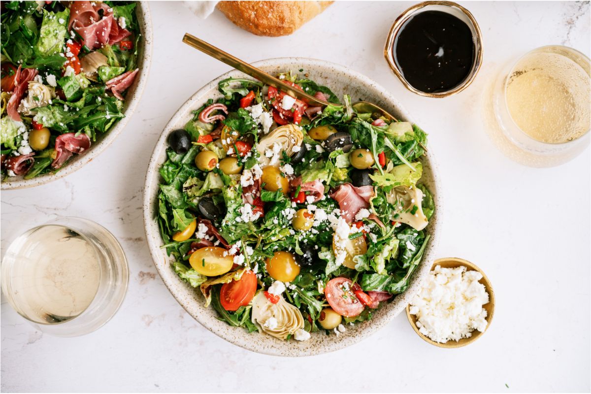 Antipasto Salad in a white bowl with a fork, remaining Antipasto Salad off to the side in a large bowl.