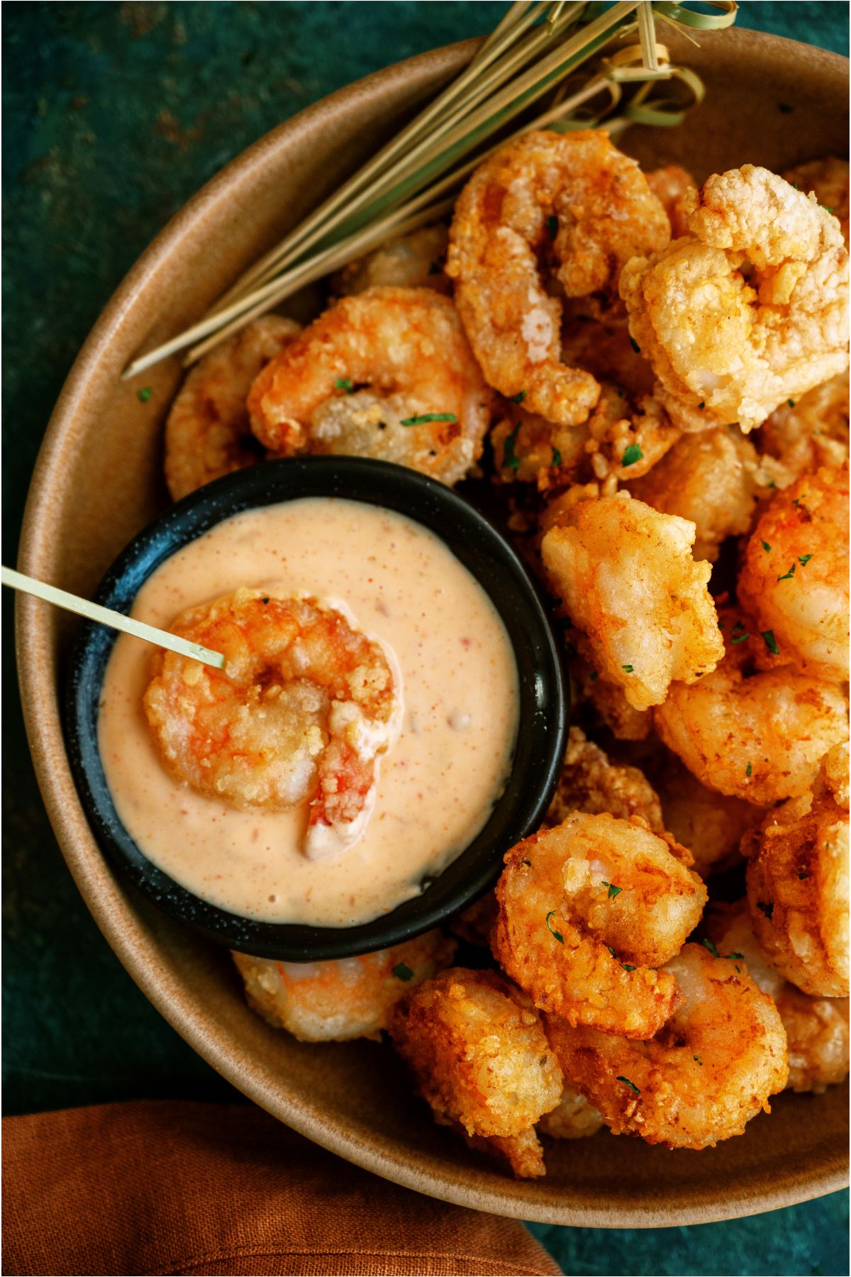 A Bang Bang Shrimp stabbed with a toothpick in a small bowl of sauce with the remaining Bang Bang Shrimp in the larger bowl.