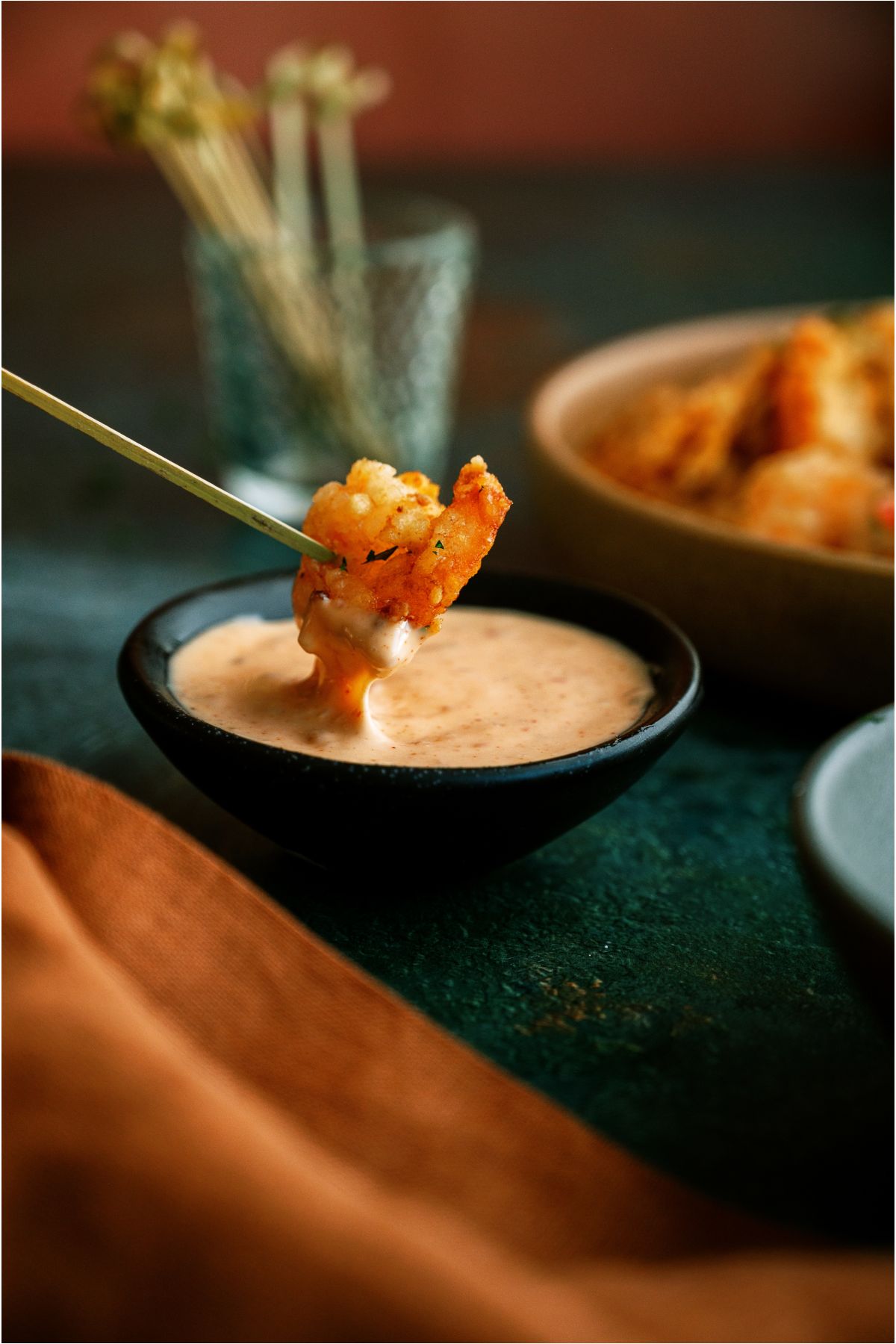 A Bang Bang Shrimp stabbed with a toothpick being dipped in a small bowl of dipping sauce.