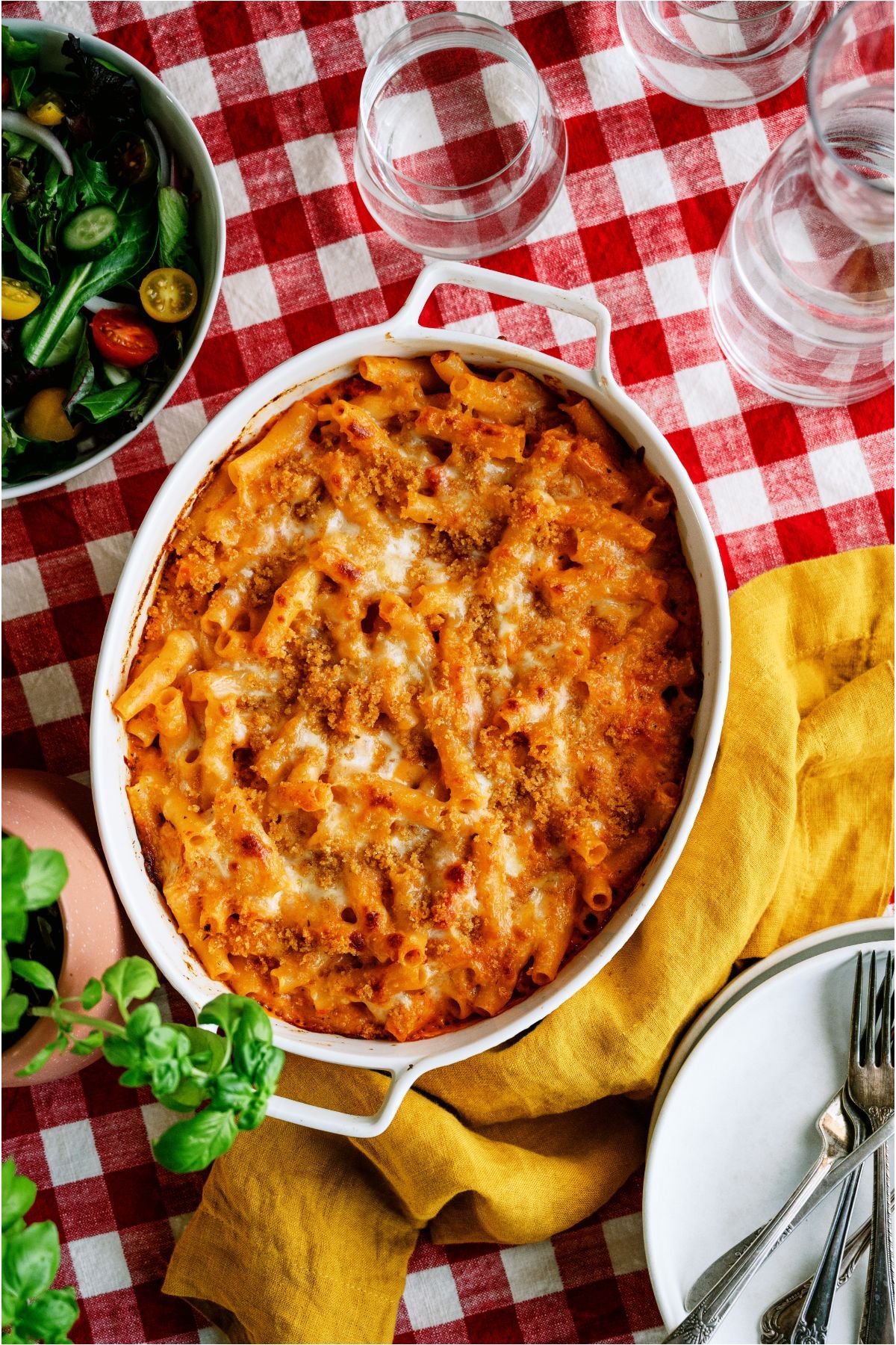 Top view of Five Cheese Ziti Al Forno in an oval baking dish on top of a red and white checkered tablecloth.