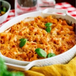 A baking dish of Five Cheese Ziti Al Forno on top of a checkered table cloth with glassware in the background.