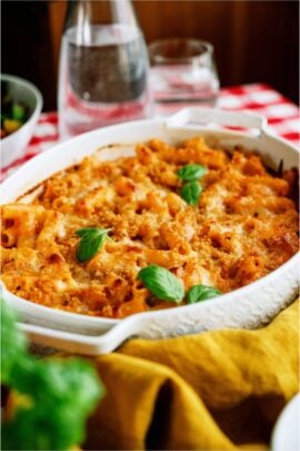 A baking dish of Five Cheese Ziti Al Forno on top of a checkered table cloth with glassware in the background.