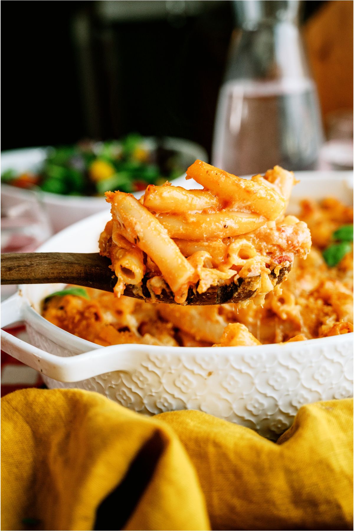 A serving spoon lifting a scoop of Five Cheese Ziti Al Forno out of the baking dish.