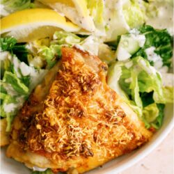 A piece of Garlic Parmesan Chicken on a plate with salad.