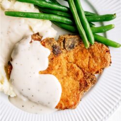 Shake And Bake Pork Chop on a white dinner plate with mashed potatoes, gravy and green beans.