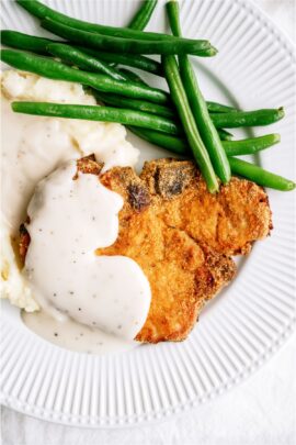 Shake And Bake Pork Chop on a white dinner plate with mashed potatoes, gravy and green beans.