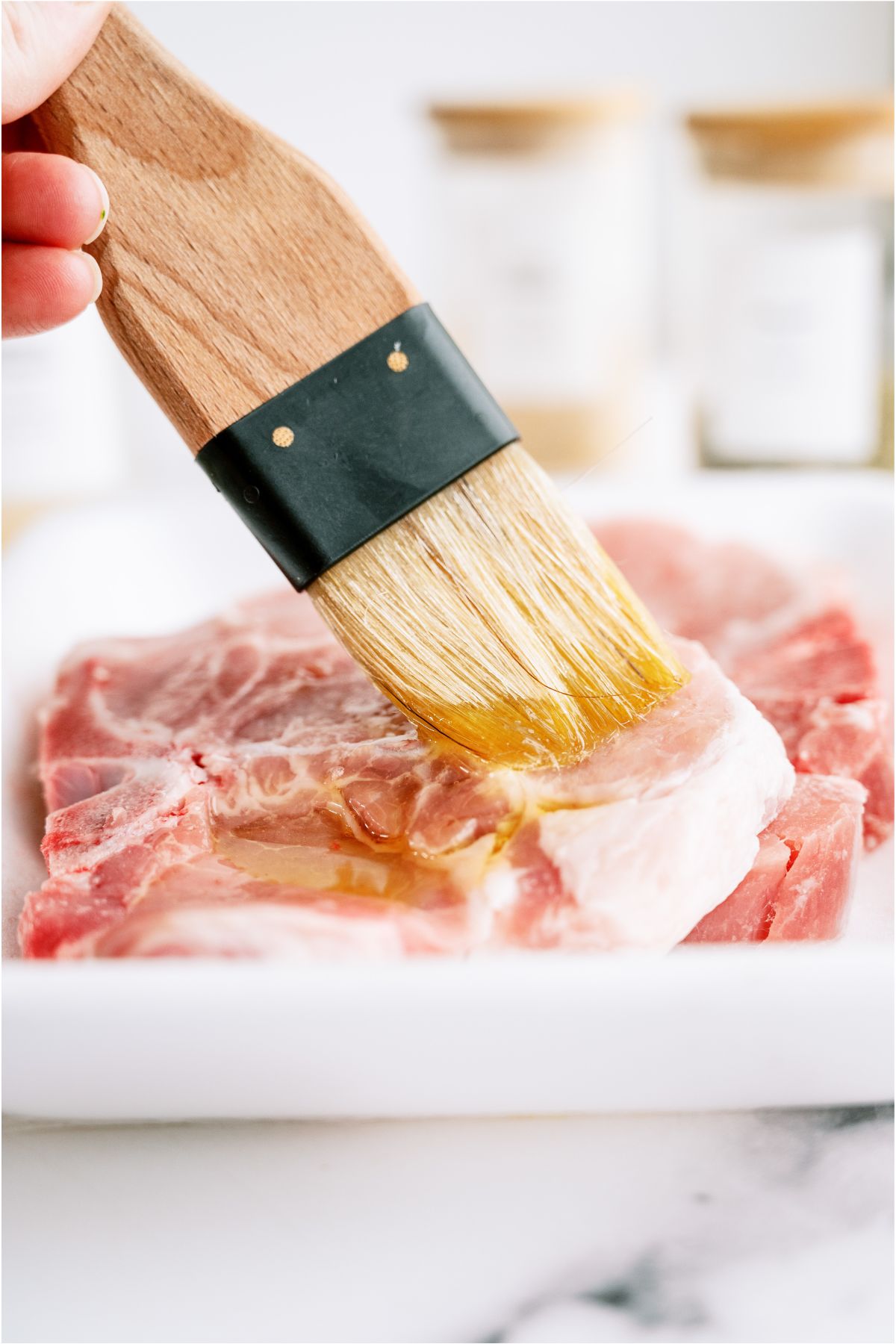 Brushing olive oil onto raw pork chop.