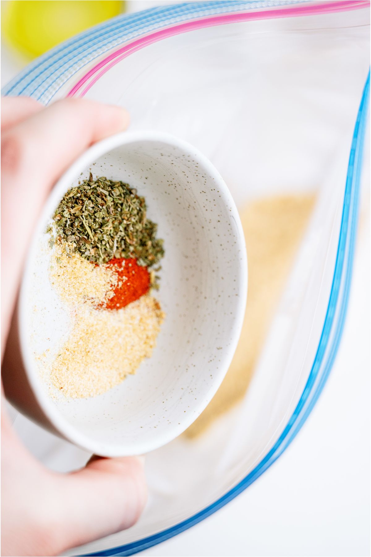 A small bowl of seasonings being poured into a ziploc bag.