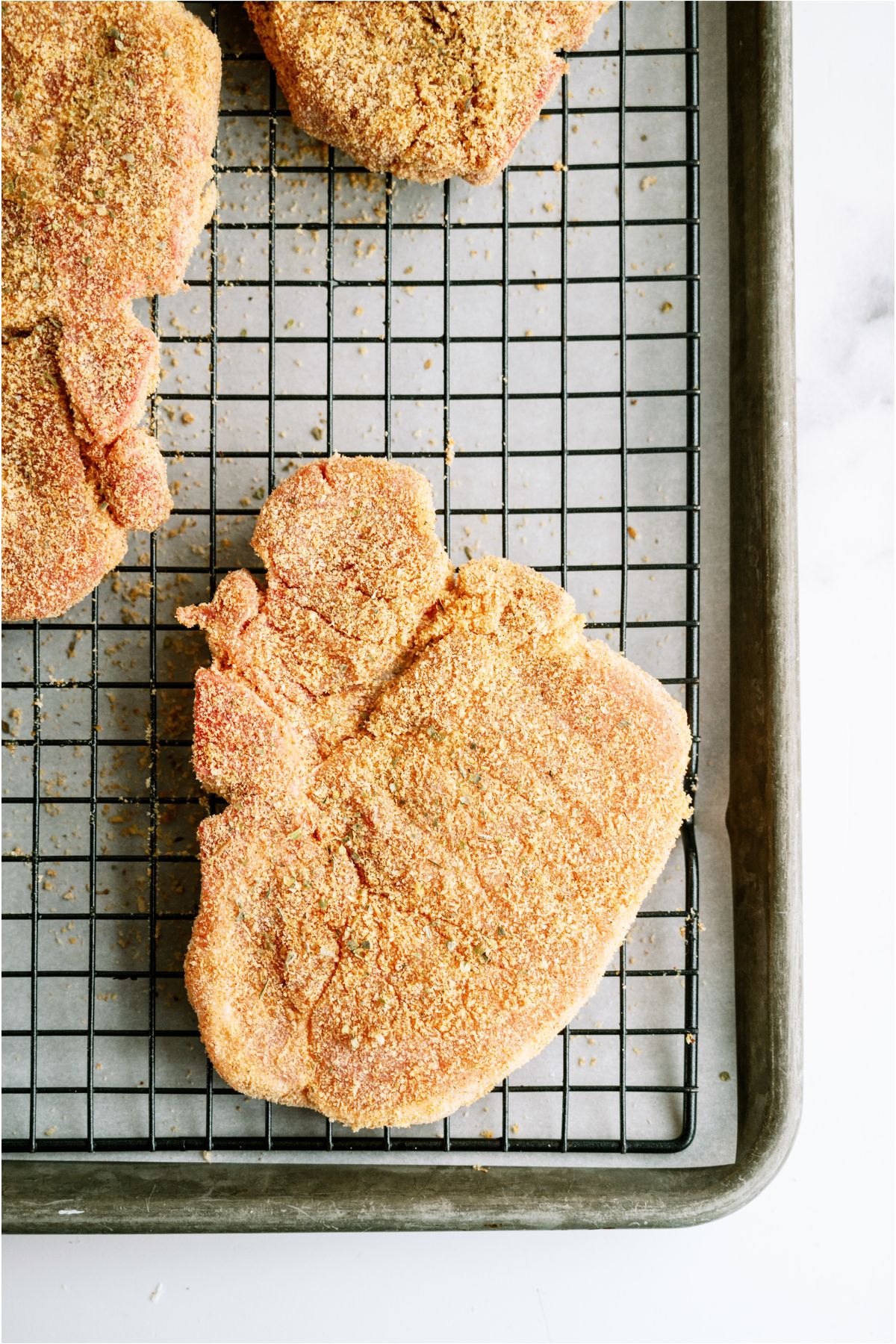 Homemade Shake And Bake Pork Chops on a wire rack over a baking sheet ready to be baked.