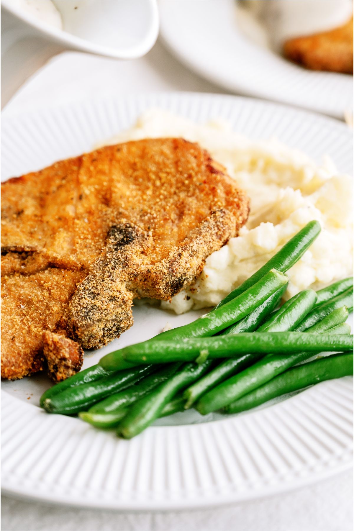 Shake And Bake Pork Chop on a white dinner plate with mashed potatoes, gravy and green beans.