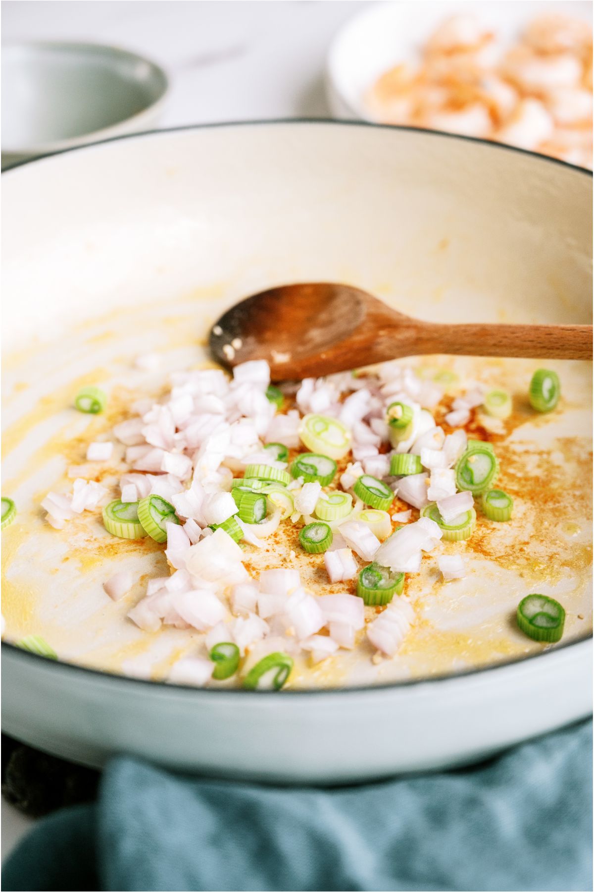 Onions and Shallots cooked in a skillet with a wooden spoon.