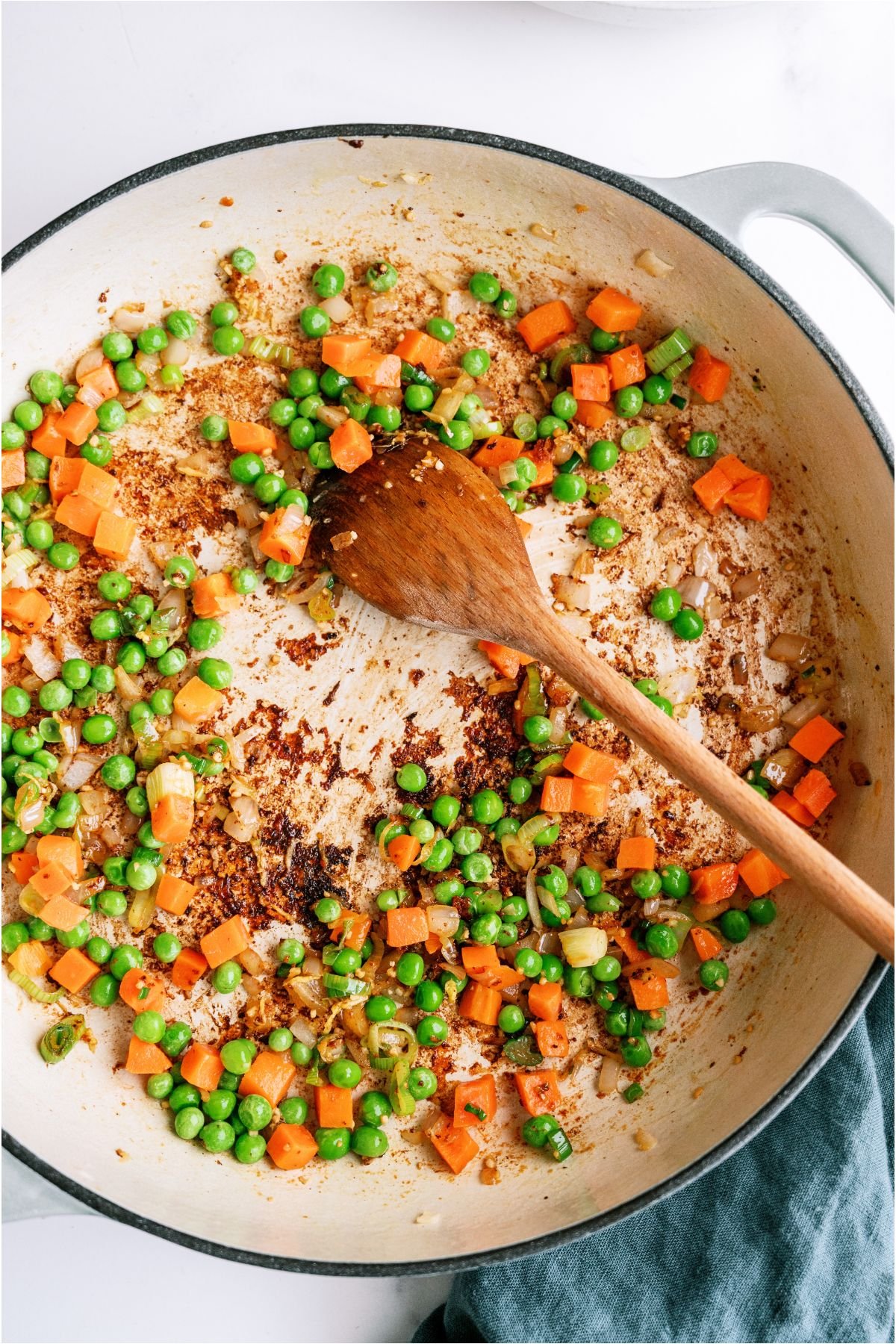 Mixed veggies cooking in a skillet with a wooden spoon.