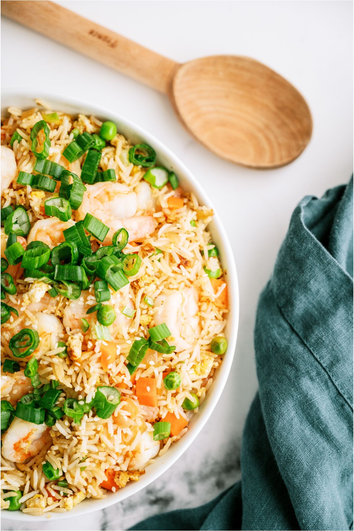 A bowl of Shrimp Fried Rice topped with green onions and a wooden spoon on the side.